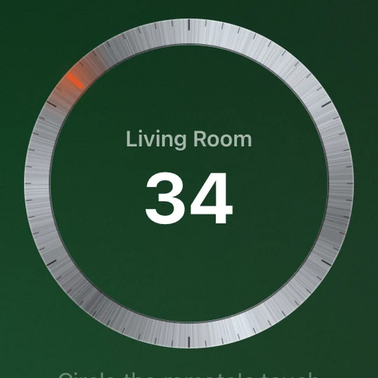 The Dial volume dial on the television: brushed steel, sixty detents, an ember tick at 34, the room name and the number in the middle